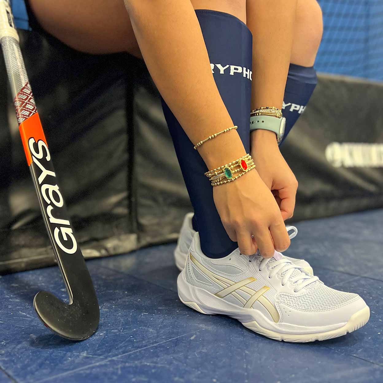 Person tying shoelaces with a hockey stick on a blue surface