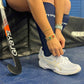 Person tying shoelaces with a hockey stick on a blue surface