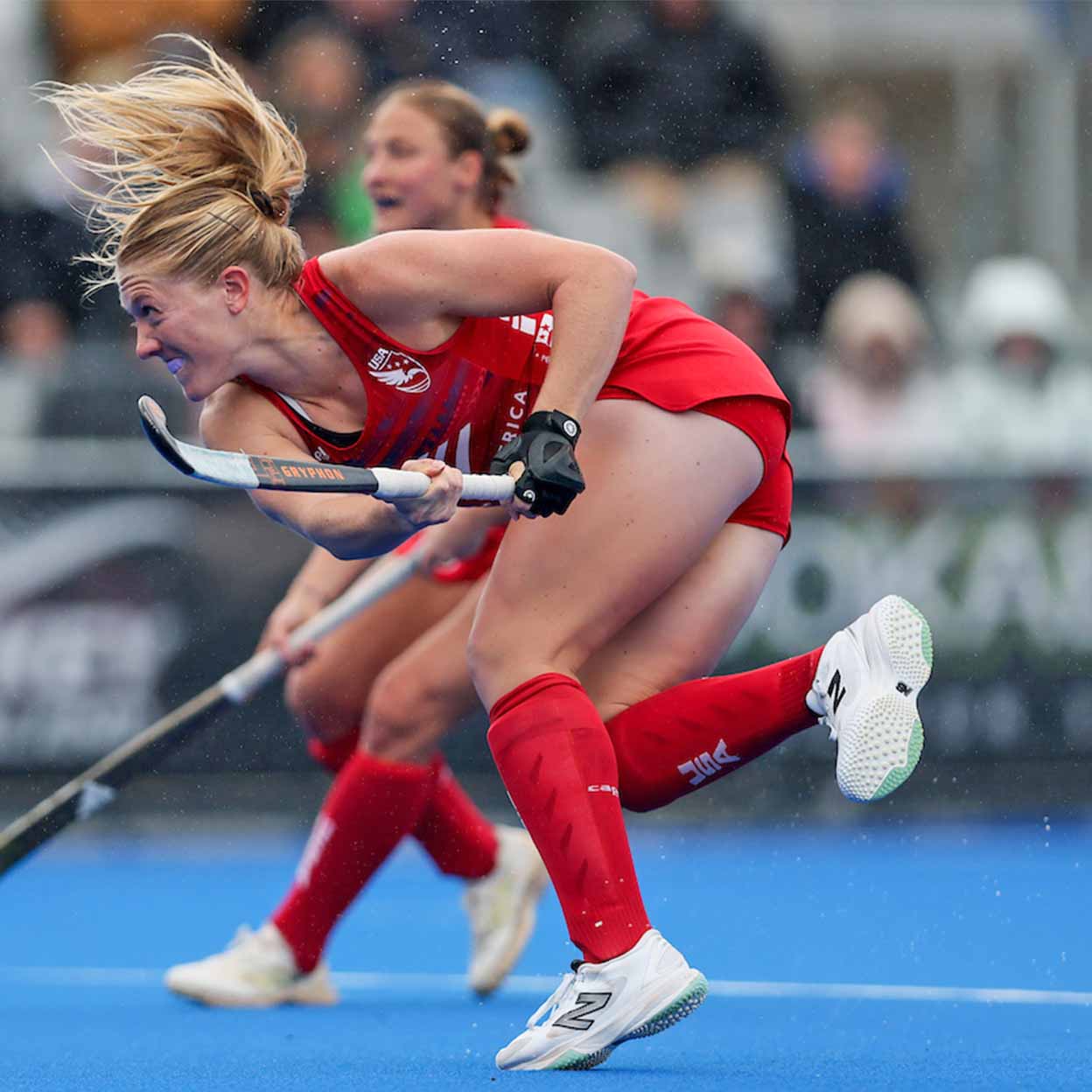 Two female hockey players in red uniforms competing on a blue field.