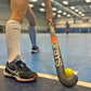 Person holding a Grays hockey stick with a yellow ball on an indoor sports court.