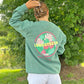 Person wearing a green sweatshirt with 'LONGSTRETH' and tropical design on the back, standing outdoors.