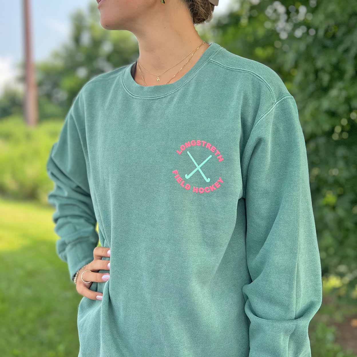 Person wearing a teal sweatshirt with a logo outdoors