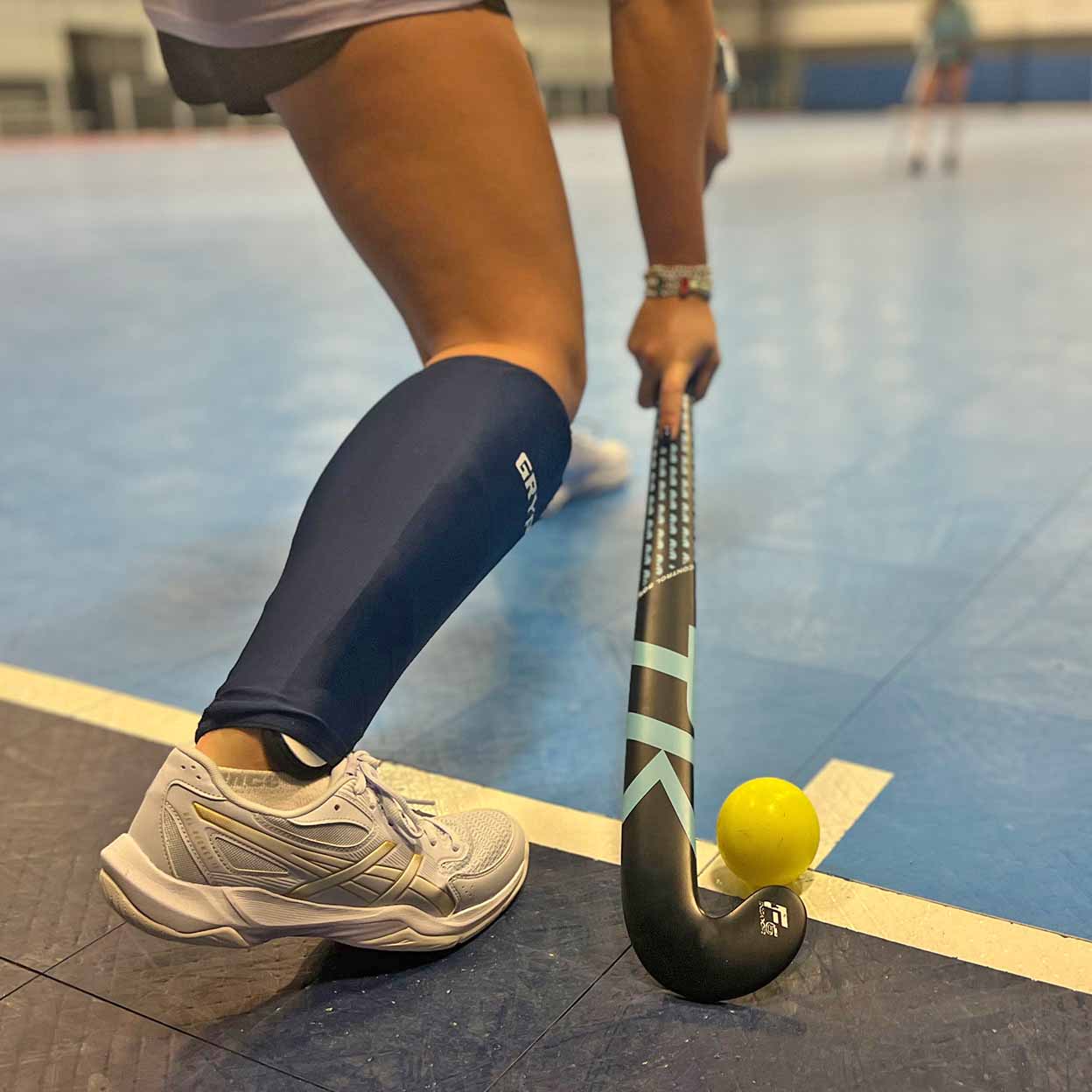 Person playing field hockey with a stick and ball on an indoor court