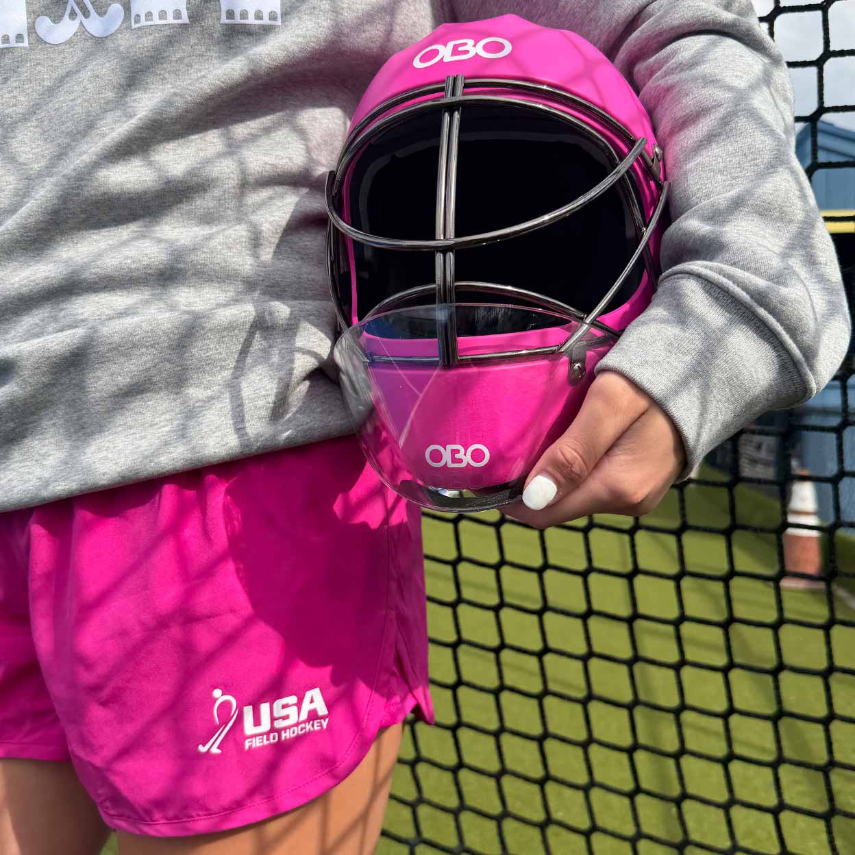 Person holding a pink helmet wearing pink shorts in front of a net. 