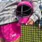 Person holding a pink helmet wearing pink shorts in front of a net. 