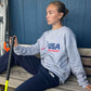 girl sitting on a bench wearing the USA Field Hockey Unisex Crewneck Sweatshirt.