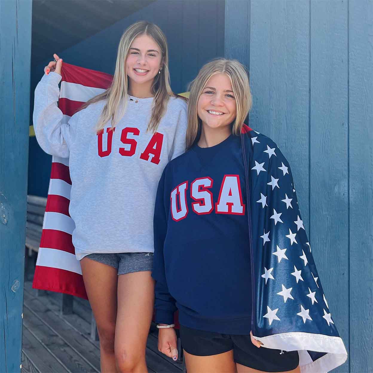 two girls with a flag wrapped around them wearing USA Field Hockey Tackle Twill Crewnecks.