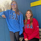 Two women wearing blue and red 'USA' sweatshirts standing against a blue wall.