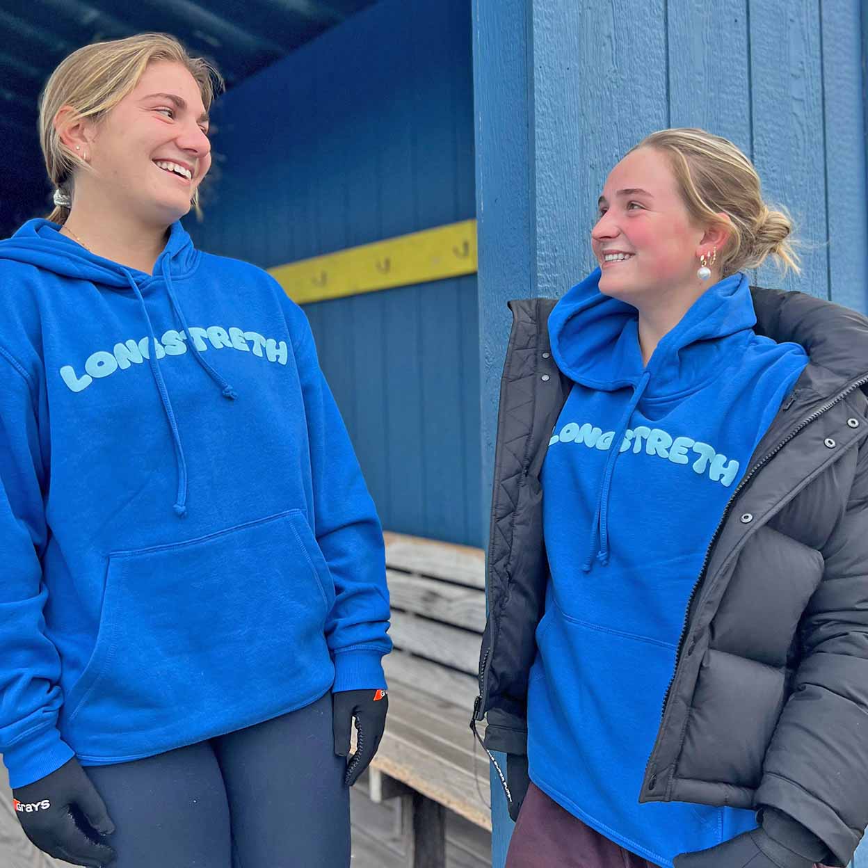 Two people wearing blue hoodies with Longstreth branding, standing in front of a blue wall.