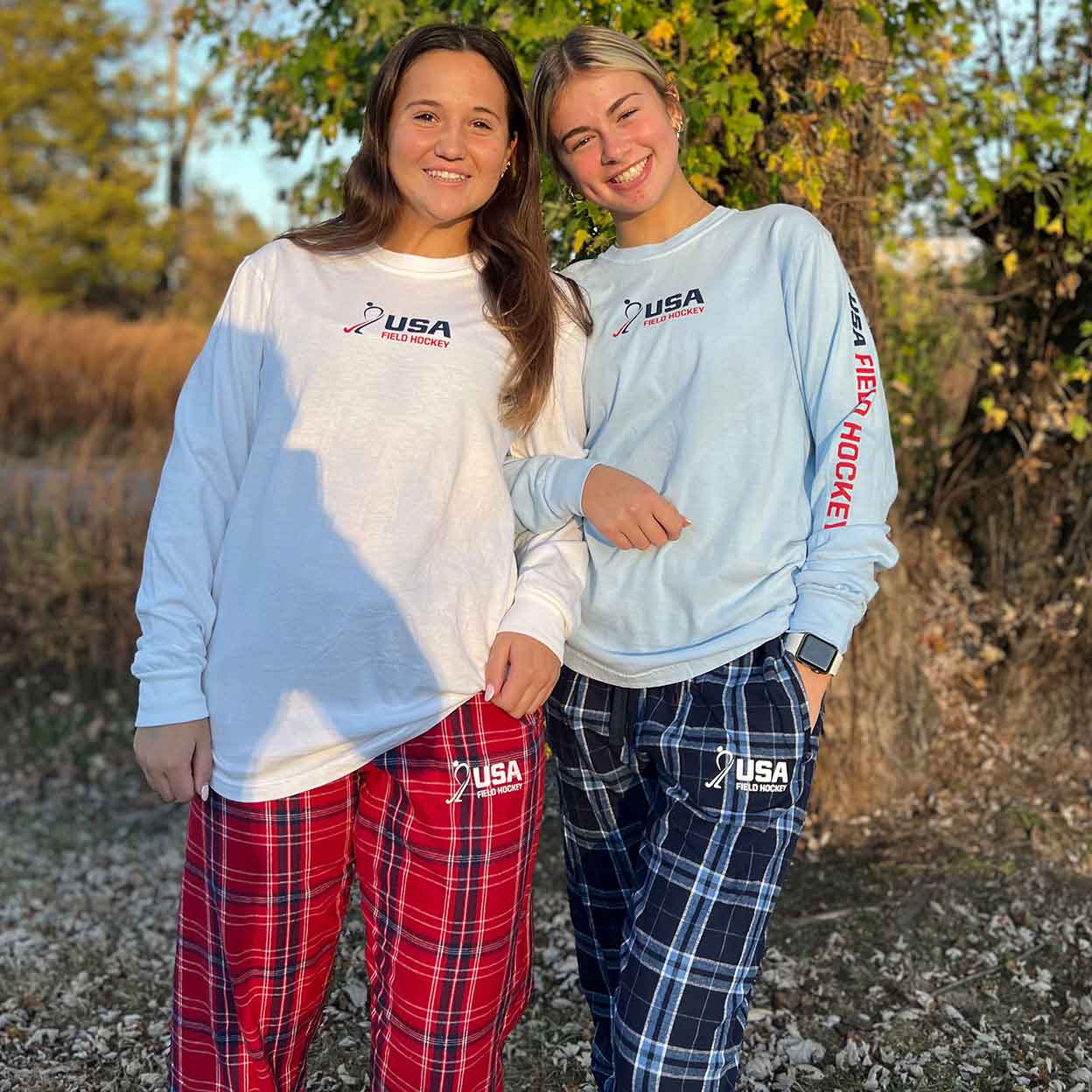 two smiling girls wearing USA field hockey tops and flannel bottoms. 