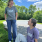 Two girls one standing one sitting. Both wearing the USA Field Hockey Heathered Tee.