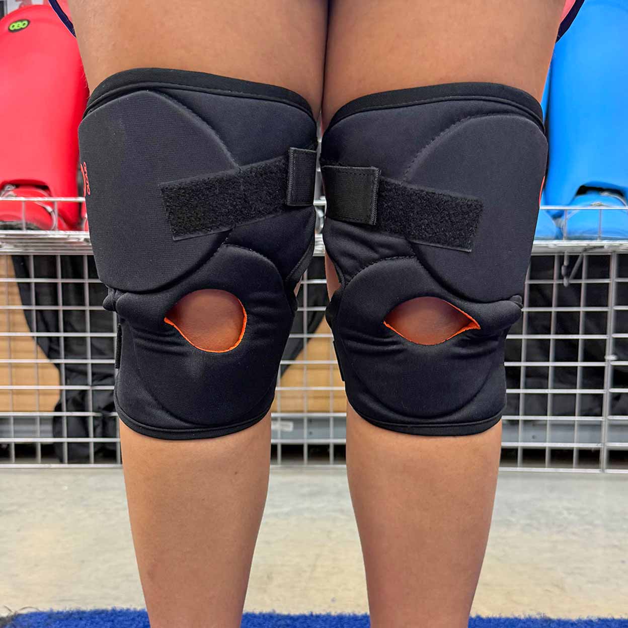 Black knee pads on a person's knees with a sports field background