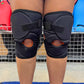 Black knee pads on a person's knees with a sports field background