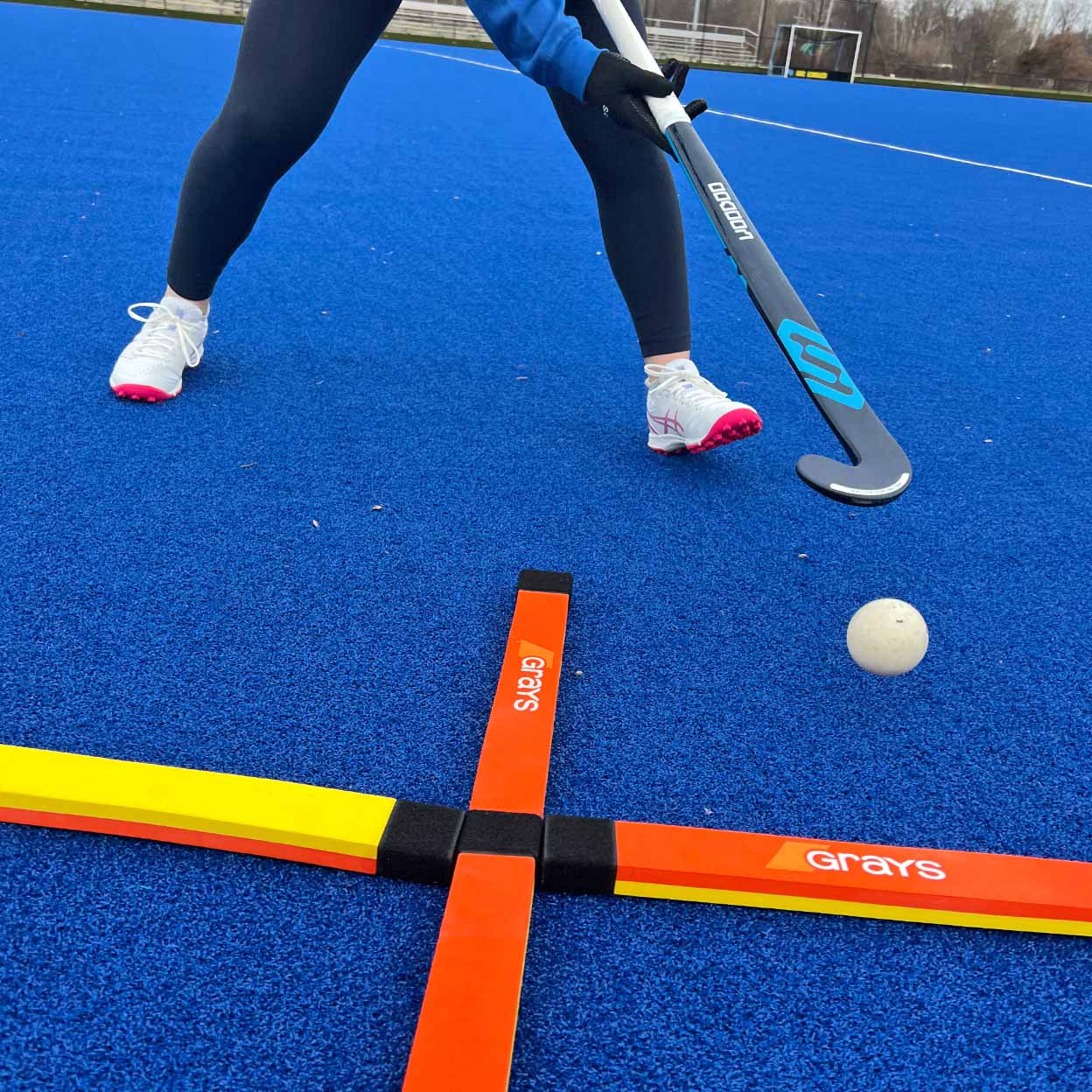 Person playing field hockey on a blue turf with equipment and ball.