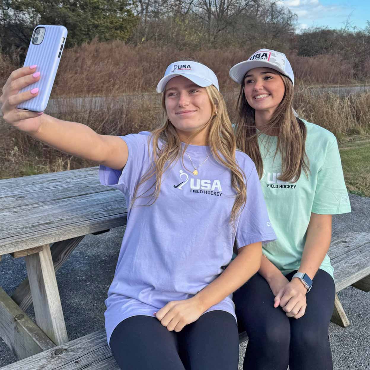 Two women taking a selfie outdoors, wearing USA Field Hockey shirts.
