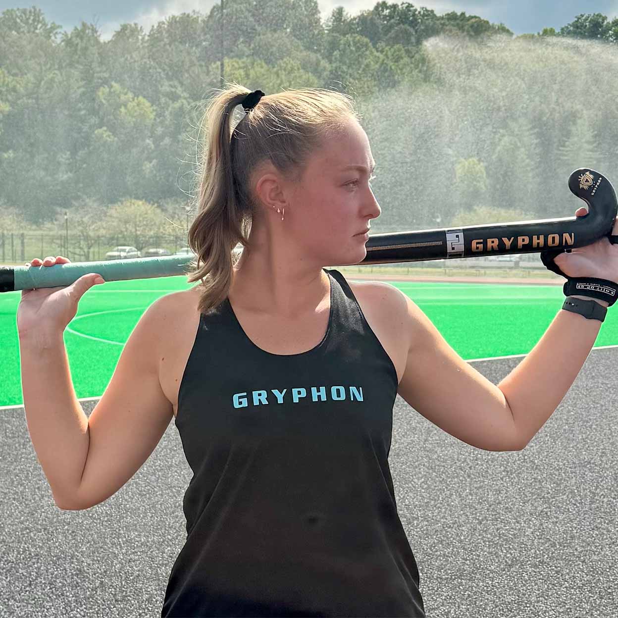 Woman holding a Gryphon field hockey stick on a sports field
