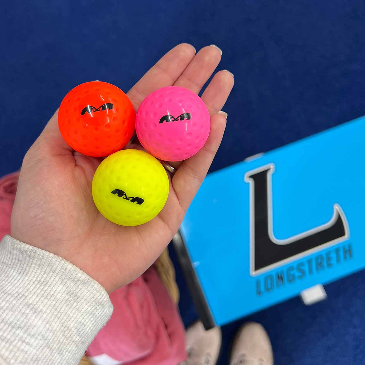 Hand holding three small balls with the Longstreth logo in the background.