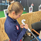 Person in a blue jacket with a logo on it, writing on sports equipment at an indoor facility.