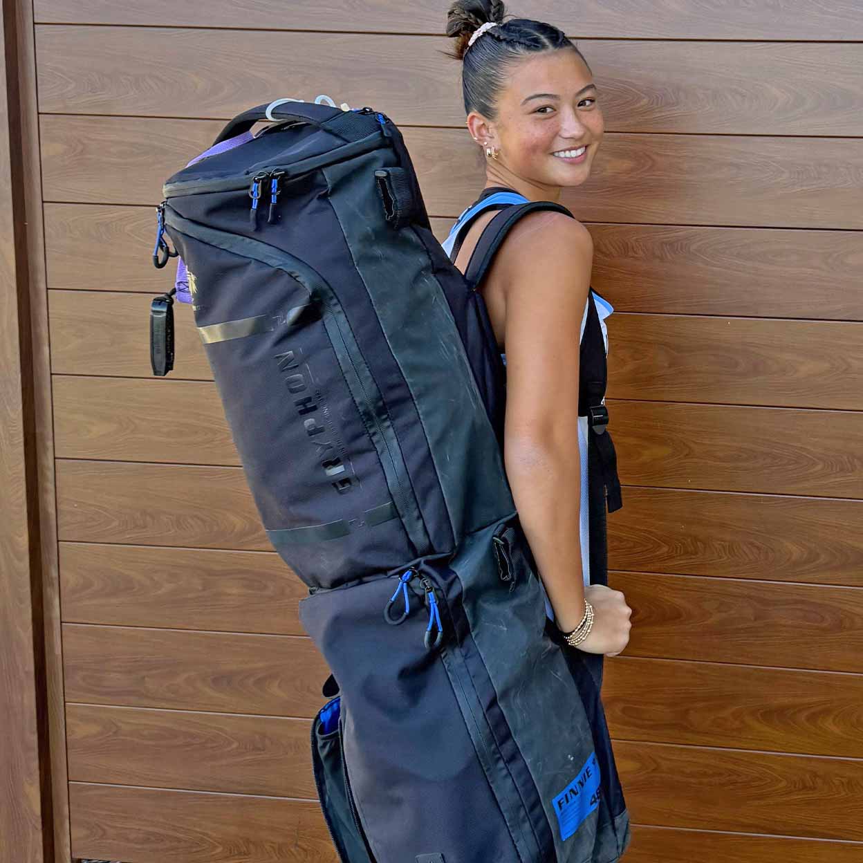 Person wearing a large black backpack against a wooden wall