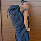 Person wearing a large black backpack against a wooden wall