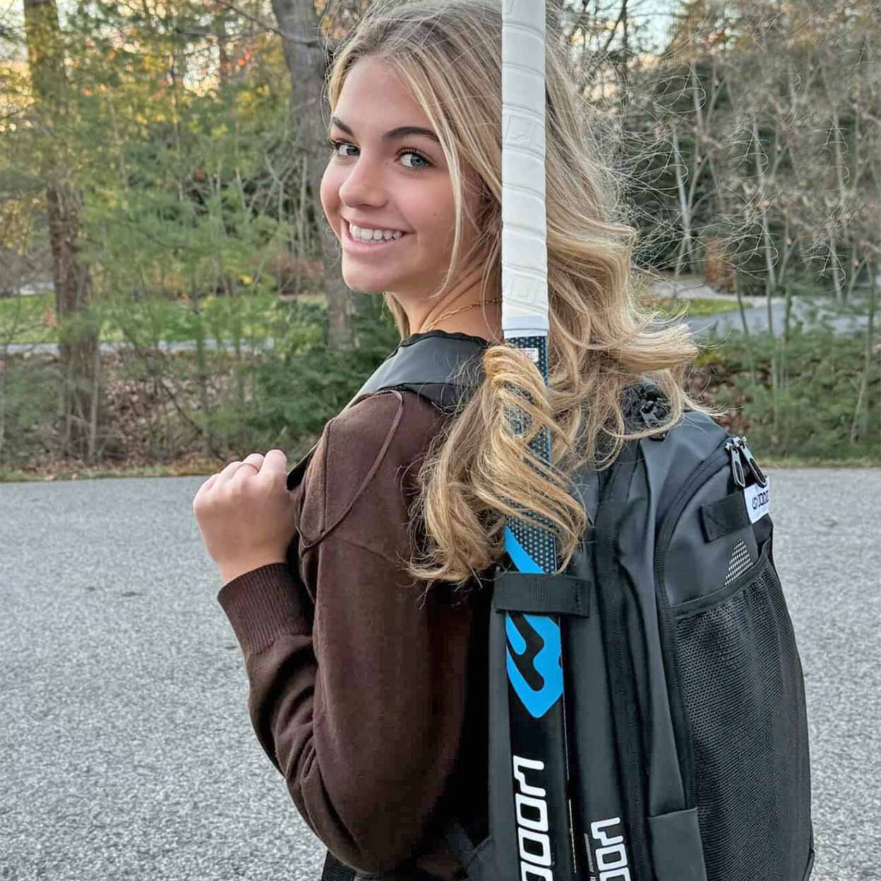 Woman holding a field hockey stick with a backpack outdoors