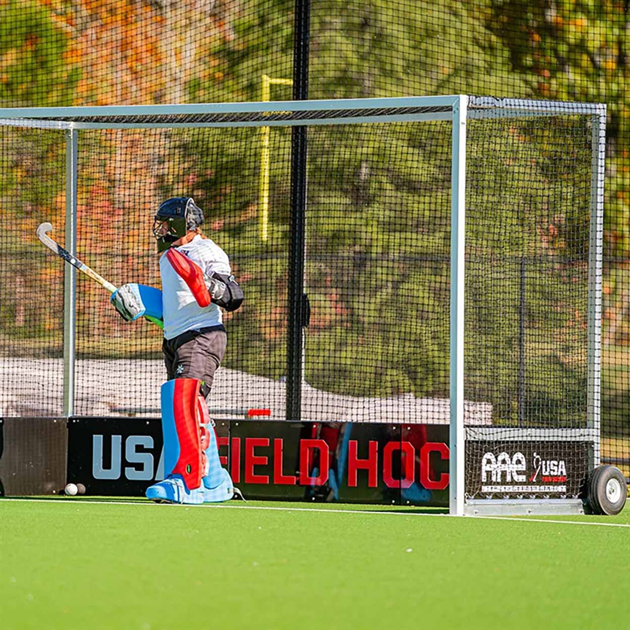 Person playing field hockey in front of a goal with 'USA Field Hockey' branding.