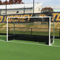 Hockey goal on a green field with a building and banners in the background
