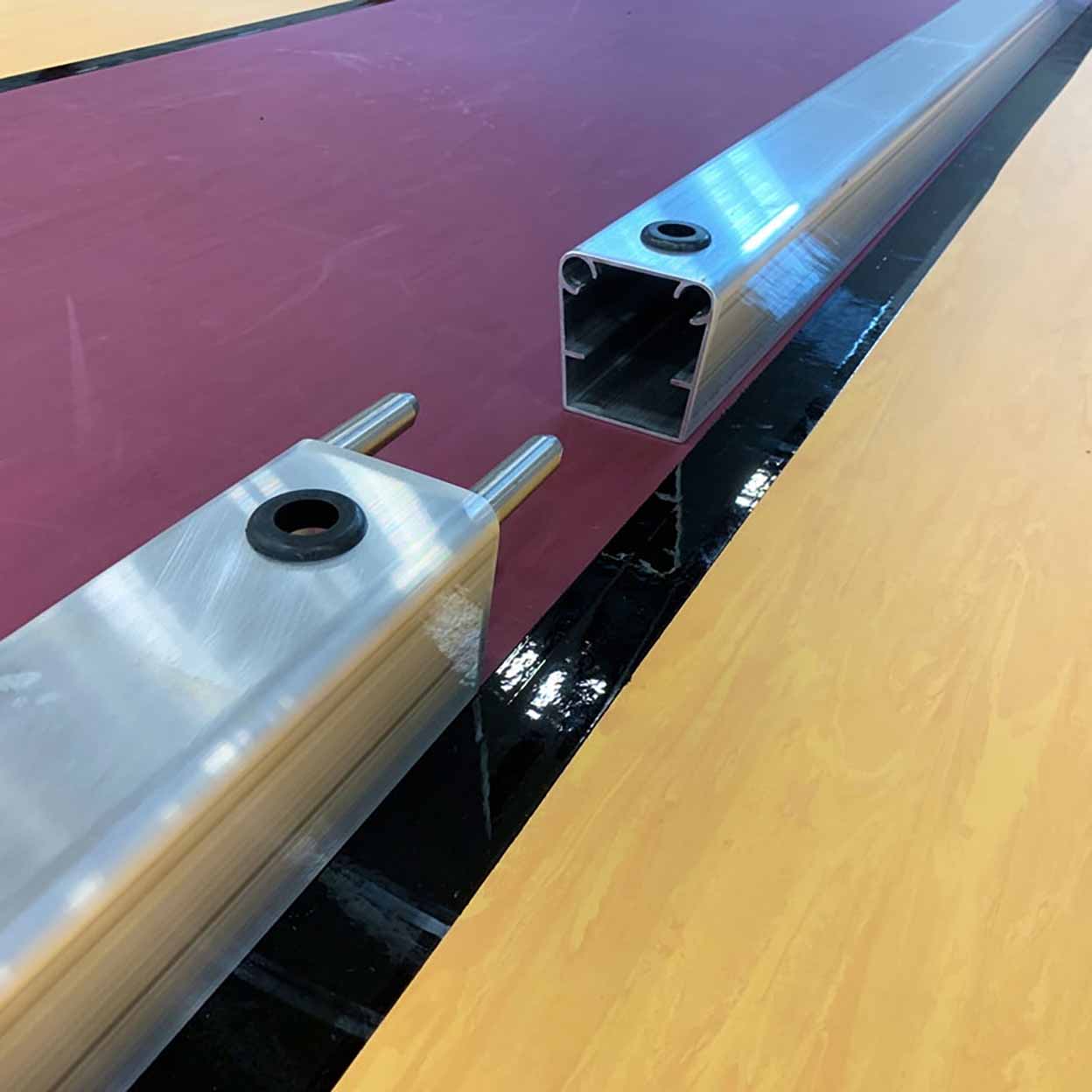 Two metal profiles on a reflective surface with a pinkish-brown background