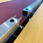Two metal profiles on a reflective surface with a pinkish-brown background