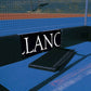 Black LANC sign on a field hockey court with blue surface and net in the background