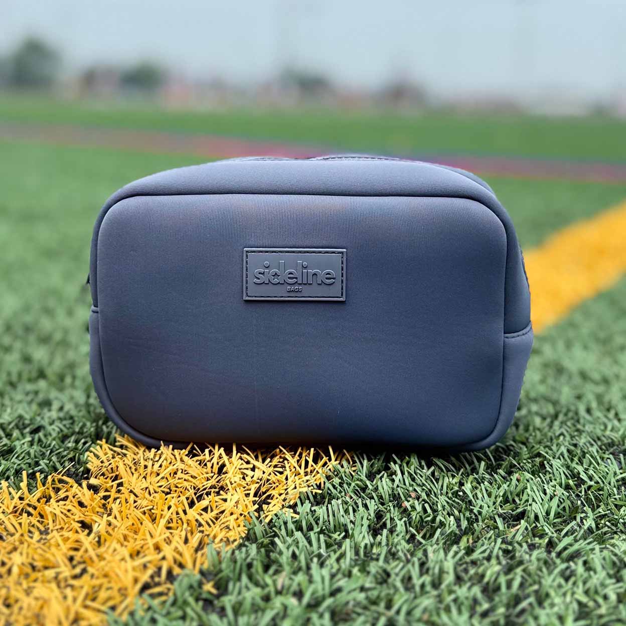 Blue toiletry bag with 'Sideline' brand on grass