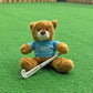 Teddy bear wearing a blue USA Field Hockey shirt with a Gryphon hockey stick on a green field background