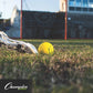 lacrosse ball on the ground about to be scooped up by a lacrosse stick.