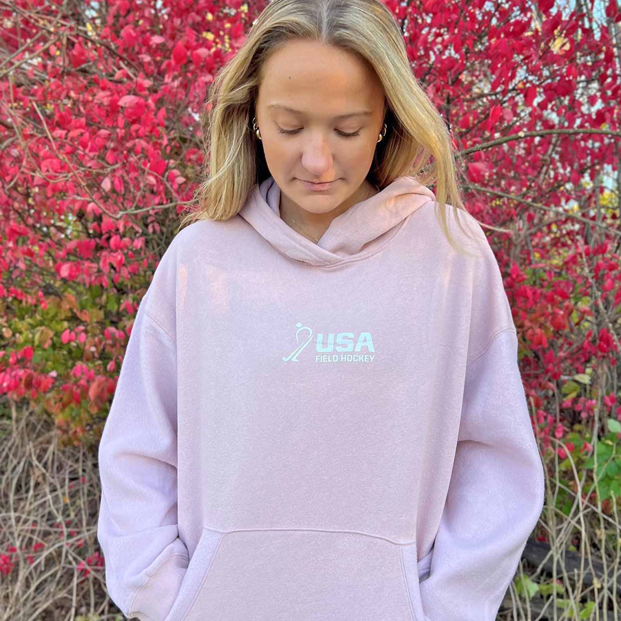 Person wearing a light purple hoodie with 'USA' logo in front of red foliage