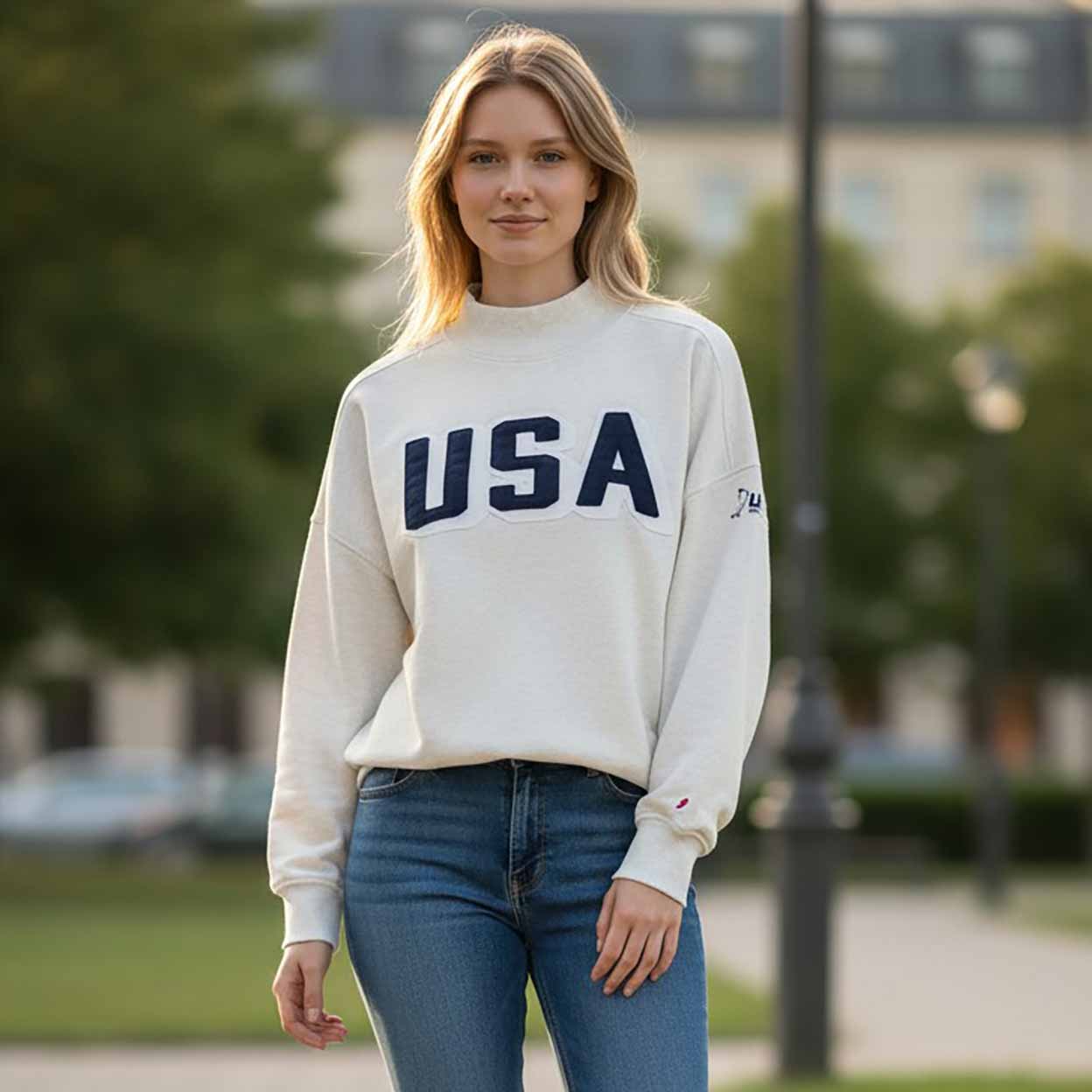 Woman wearing a white sweatshirt with 'USA' printed on it, standing outdoors.