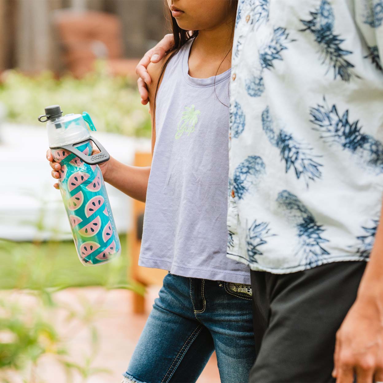 Young girl holding a O2 Cool Mist N Sip Water Bottle while her dad has his arm around her shoulder.