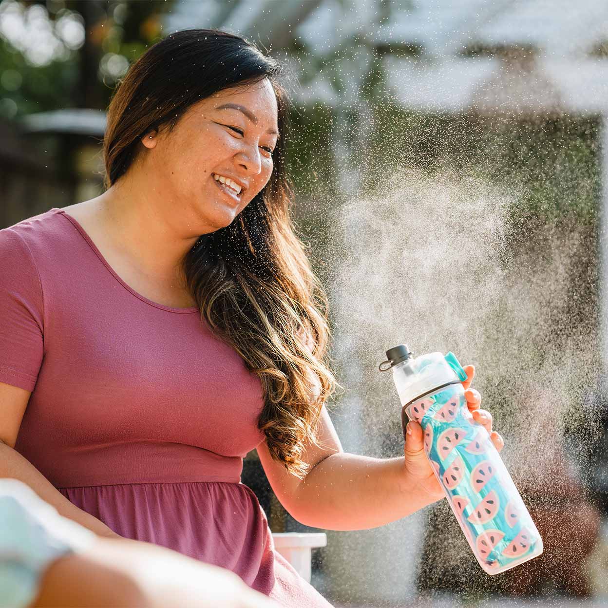 A smiling lady misting herself with a O2 Cool Mist N Sip Water Bottle