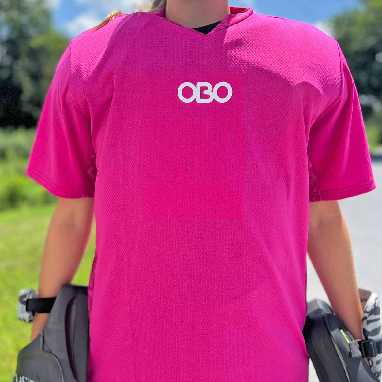 Person wearing a bright pink goalie jersey with 'OBO' logo outdoors