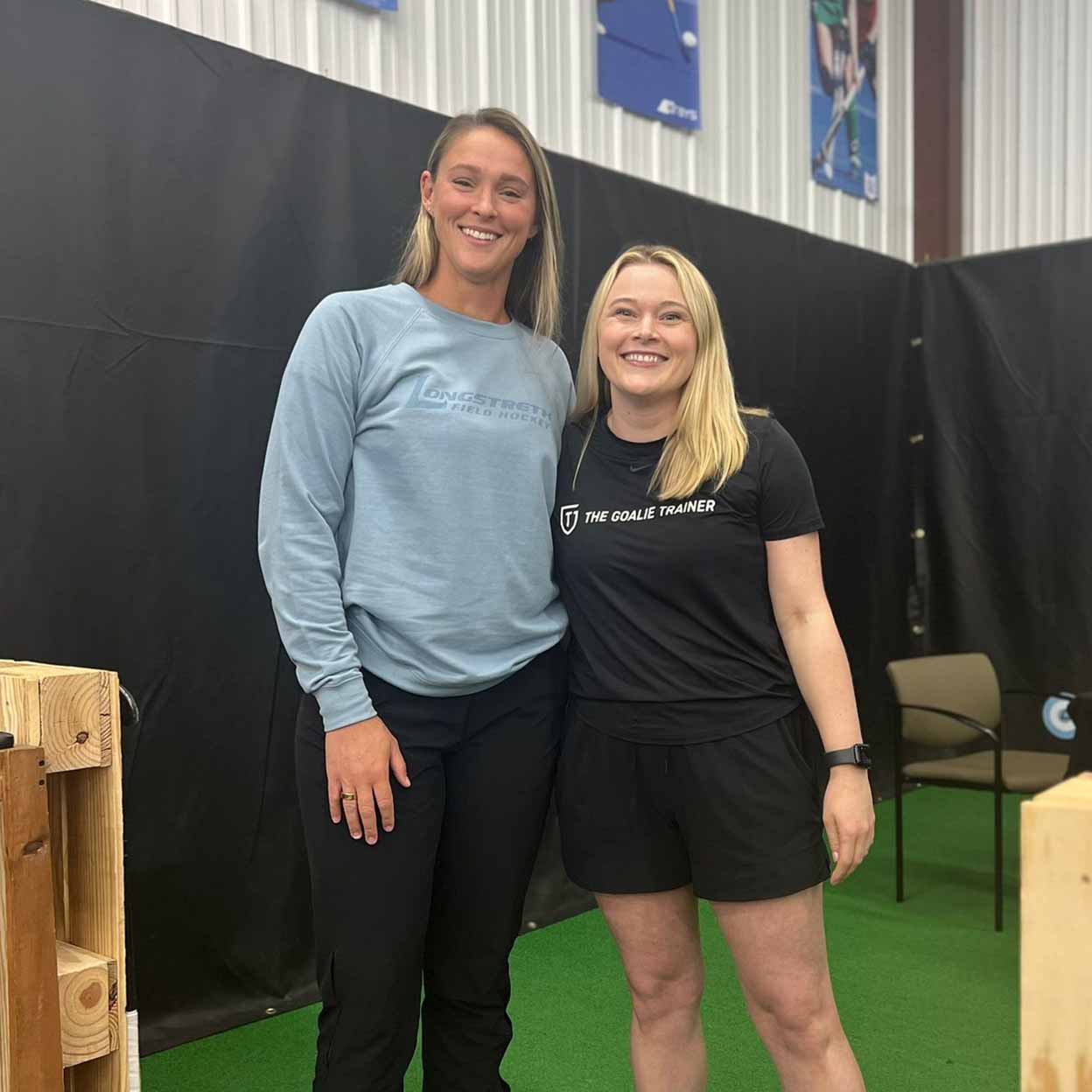 Two women standing together in an indoor setting with a black backdrop