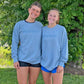 Two people wearing matching blue sweatshirts with a logo in front of green foliage.