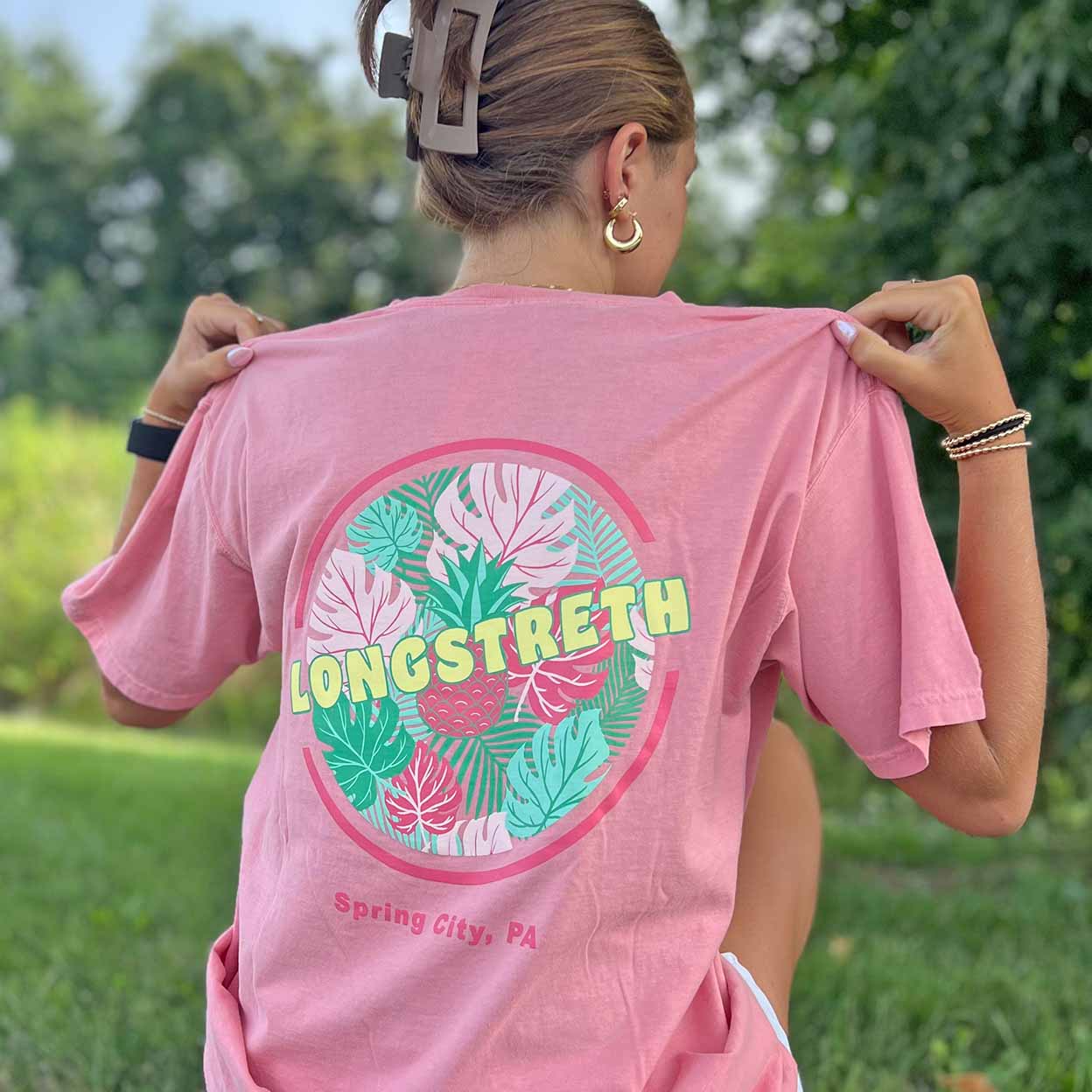 Person wearing a pink t-shirt with 'LONGSTRETH Spring City, PA' design outdoors.