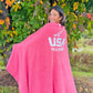 Person wrapped in a pink blanket with 'USA Field Hockey' text, standing outdoors among trees with autumn leaves.