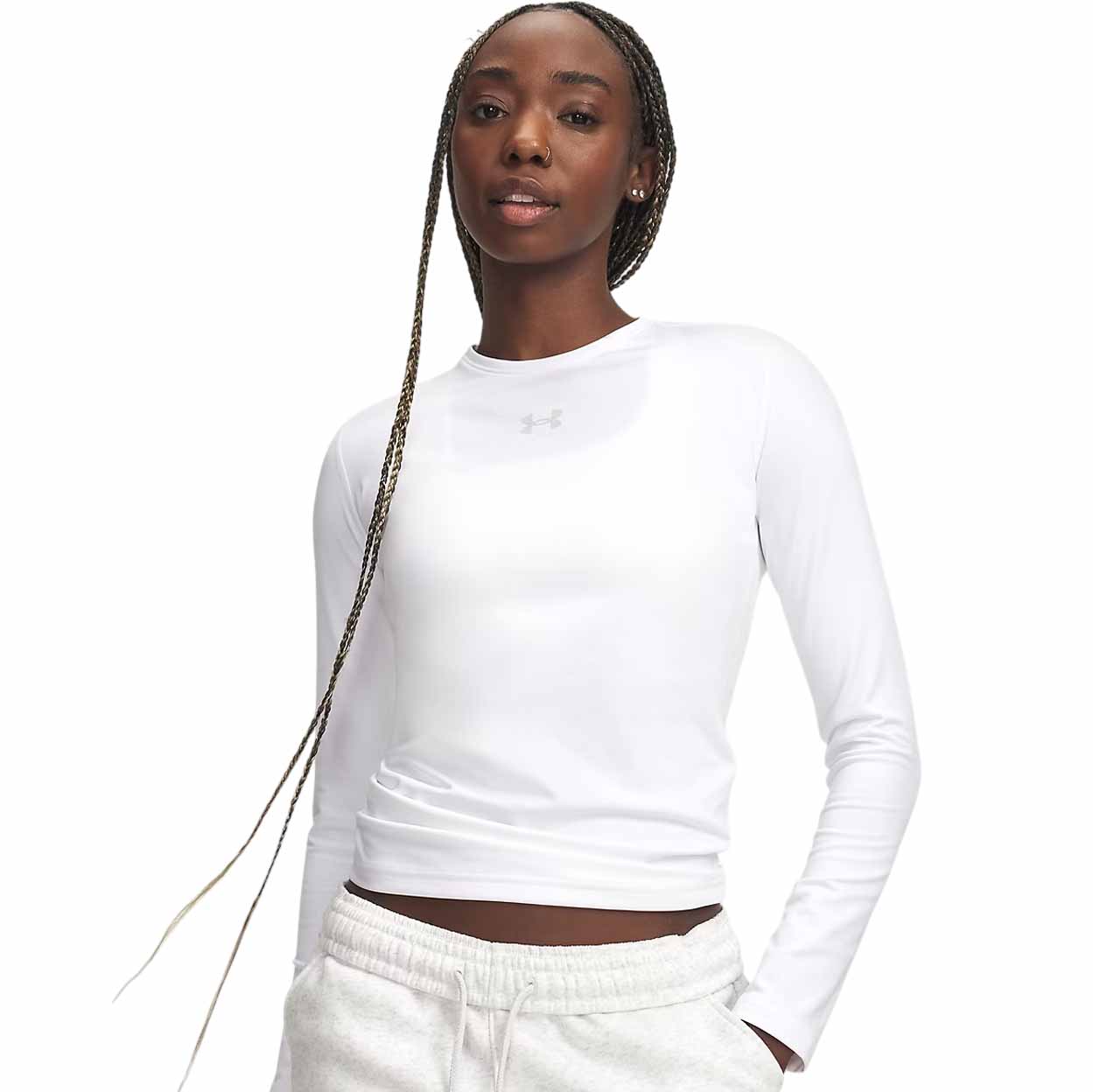 A woman modeling a fitted white long-sleeve athletic top with a small Under Armour logo on the chest, paired with white sweatpants against a plain white background.