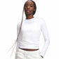 A woman modeling a fitted white long-sleeve athletic top with a small Under Armour logo on the chest, paired with white sweatpants against a plain white background.