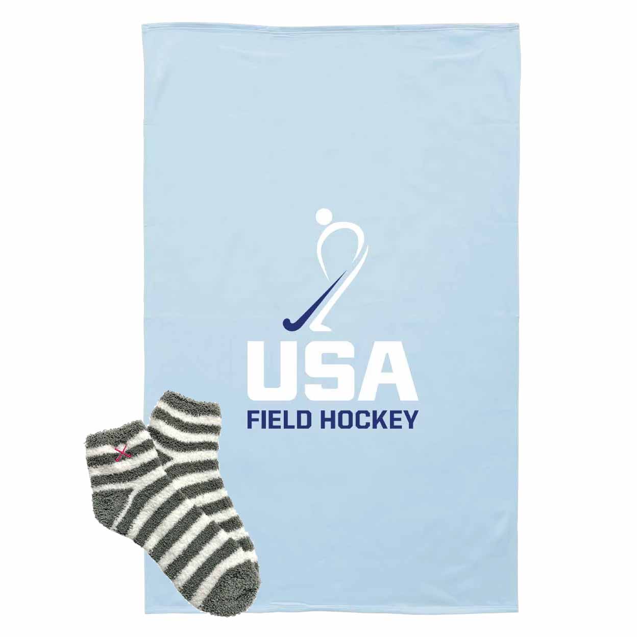 A light blue blanket featuring the USA Field Hockey logo, shown with a pair of gray and white striped socks on a plain white background.