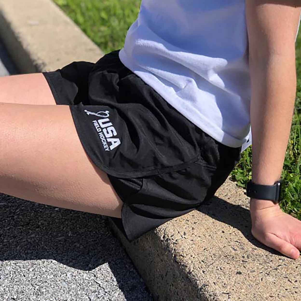 Girl sitting on a curb wearing the USA Field Hockey Wayfarer Shorts.