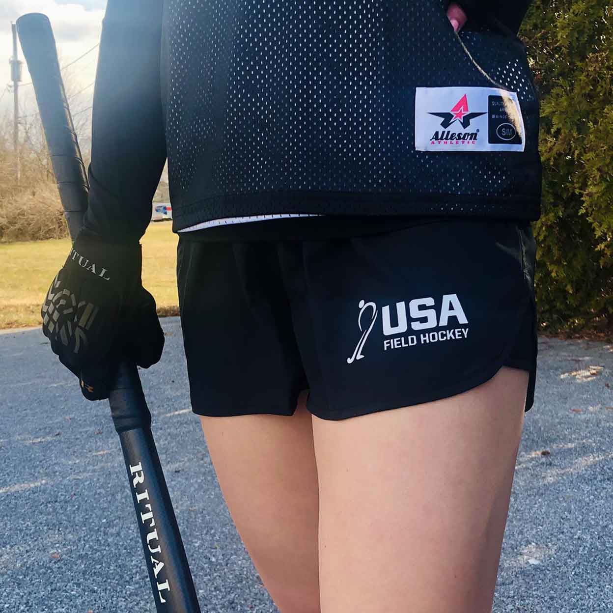 Girl wearing the USA Field Hockey Wayfarer Shorts with a field hockey stick in one hand.