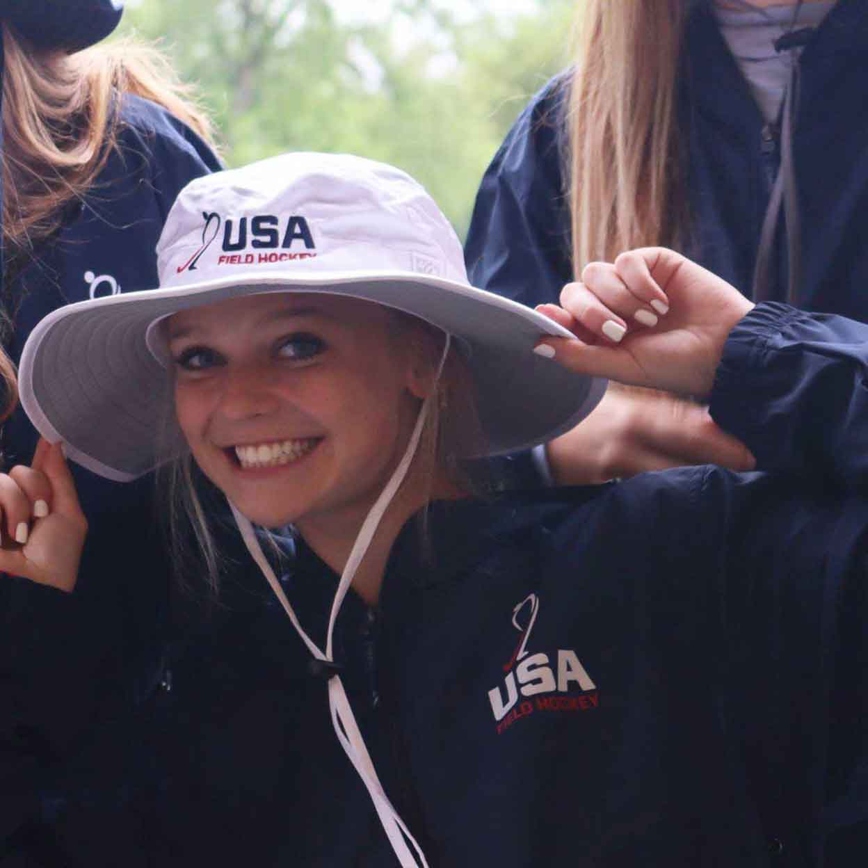 Smiling girl wearing the USA Field Hockey Boonie Hat with both hands on the brim.